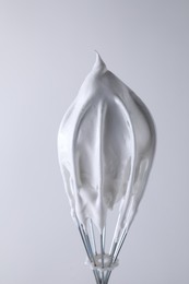 Photo of Whisk with whipped cream on white background, closeup