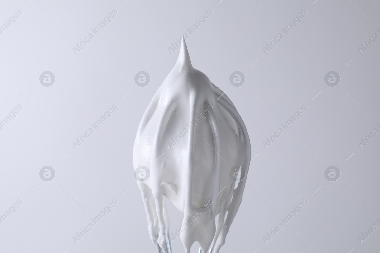 Photo of Whisk with whipped cream on white background, closeup