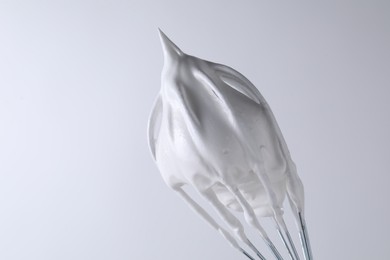 Photo of Whisk with whipped cream on white background, closeup. Space for text