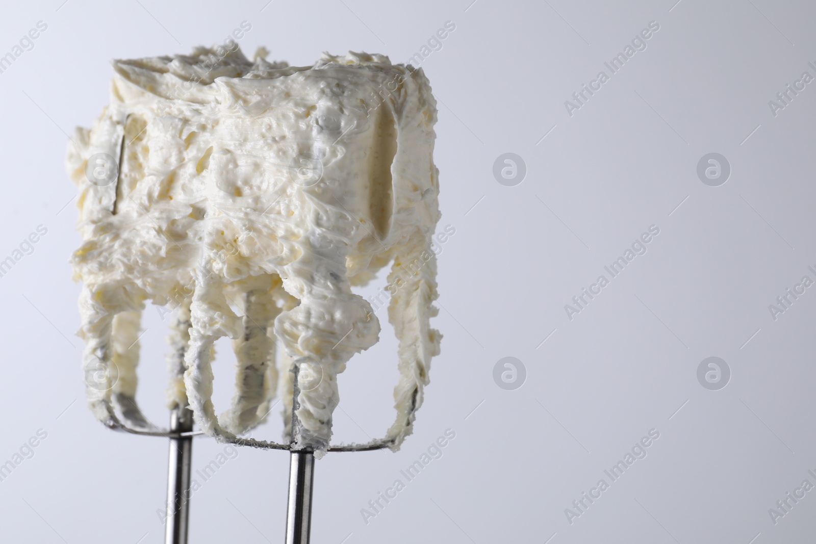 Photo of Whisks with whipped cream on white background, closeup. Space for text