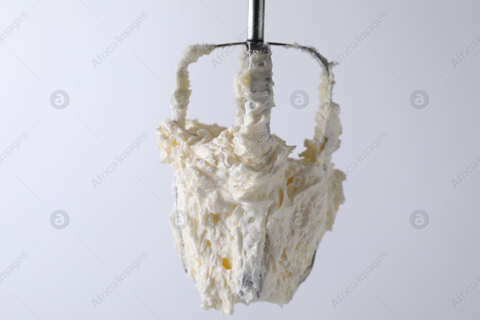 Photo of Whisk with whipped cream on white background, closeup