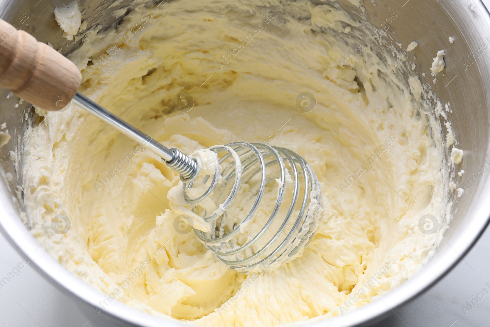 Photo of Whisking whipped cream in bowl on white table, closeup