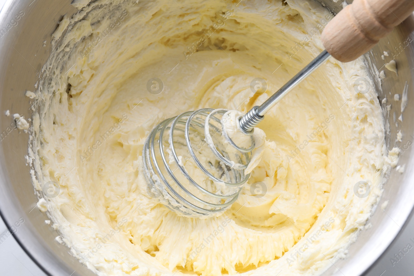 Photo of Whisking whipped cream in bowl on white table, top view