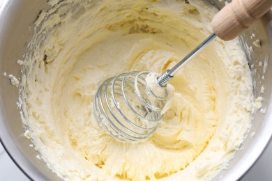 Photo of Whisking whipped cream in bowl on white table, top view