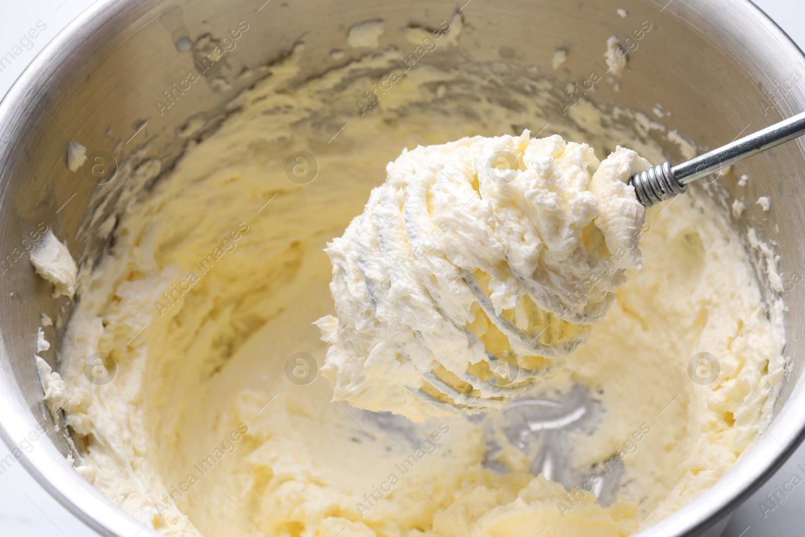 Photo of Whisking whipped cream in bowl on white table, closeup