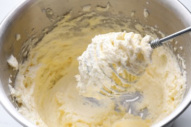 Photo of Whisking whipped cream in bowl on white table, closeup