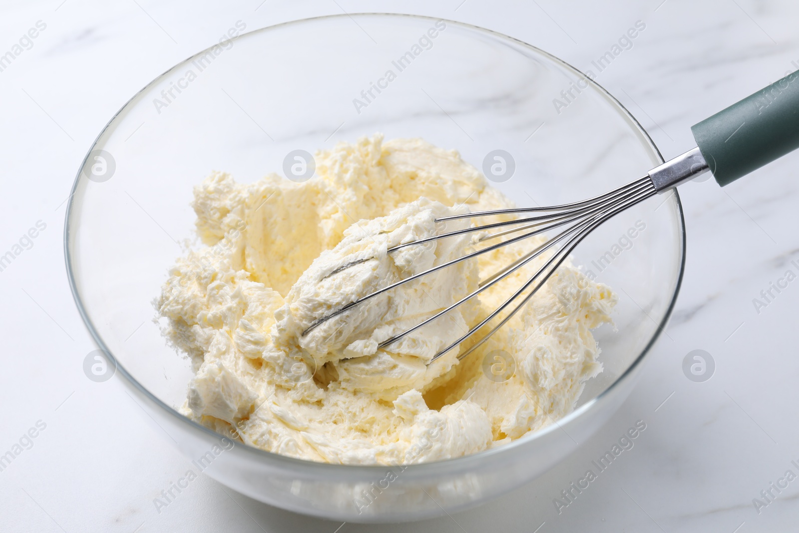 Photo of Bowl with whisk and whipped cream on white marble table, closeup