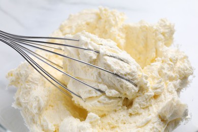 Photo of Bowl with whisk and whipped cream on white table, closeup