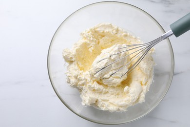 Photo of Bowl with whisk and whipped cream on white marble table, top view