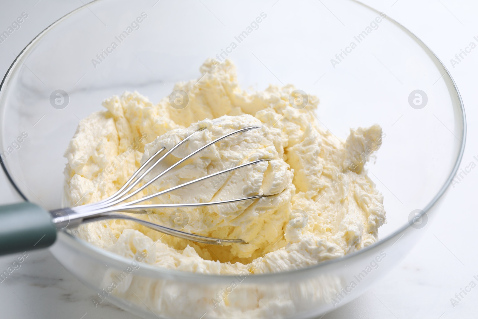 Photo of Bowl with whisk and whipped cream on white marble table, closeup