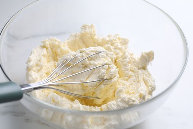 Photo of Bowl with whisk and whipped cream on white marble table, closeup