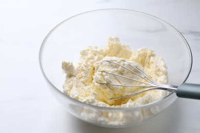 Photo of Bowl with whisk and whipped cream on white marble table, closeup