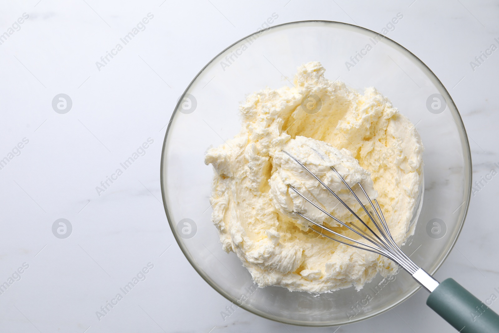 Photo of Bowl with whisk and whipped cream on white marble table, top view. Space for text