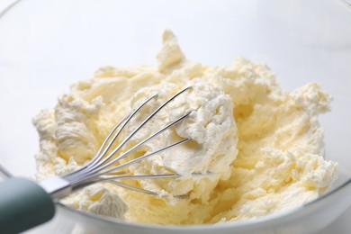 Photo of Bowl with whisk and whipped cream on white table, closeup