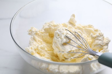 Photo of Bowl with whisk and whipped cream on white table, closeup