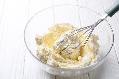 Photo of Bowl with whisk and whipped cream on white wooden table, closeup