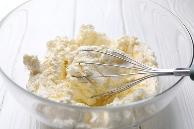 Photo of Bowl with whisk and whipped cream on white wooden table, closeup