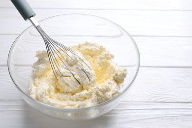 Photo of Bowl with whisk and whipped cream on white wooden table