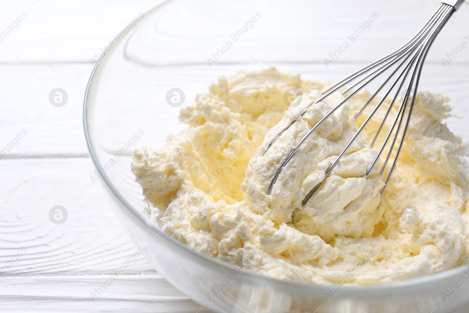 Photo of Bowl with whisk and whipped cream on white wooden table, closeup