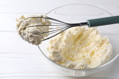 Photo of Bowl with whisk and whipped cream on white wooden table, closeup