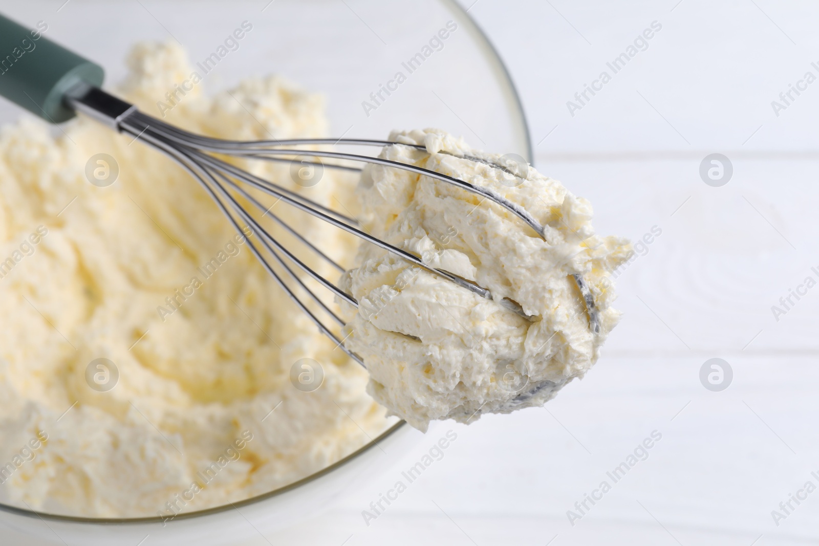 Photo of Bowl with whisk and whipped cream on white table, closeup