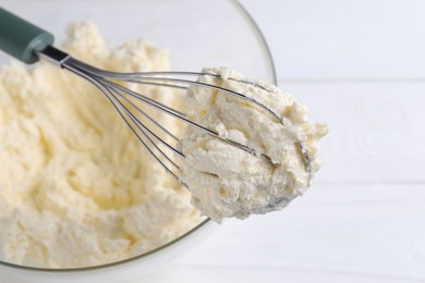 Photo of Bowl with whisk and whipped cream on white table, closeup