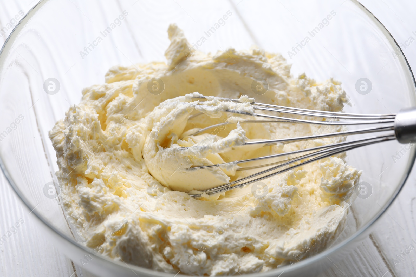 Photo of Bowl with whisk and whipped cream on white wooden table, closeup