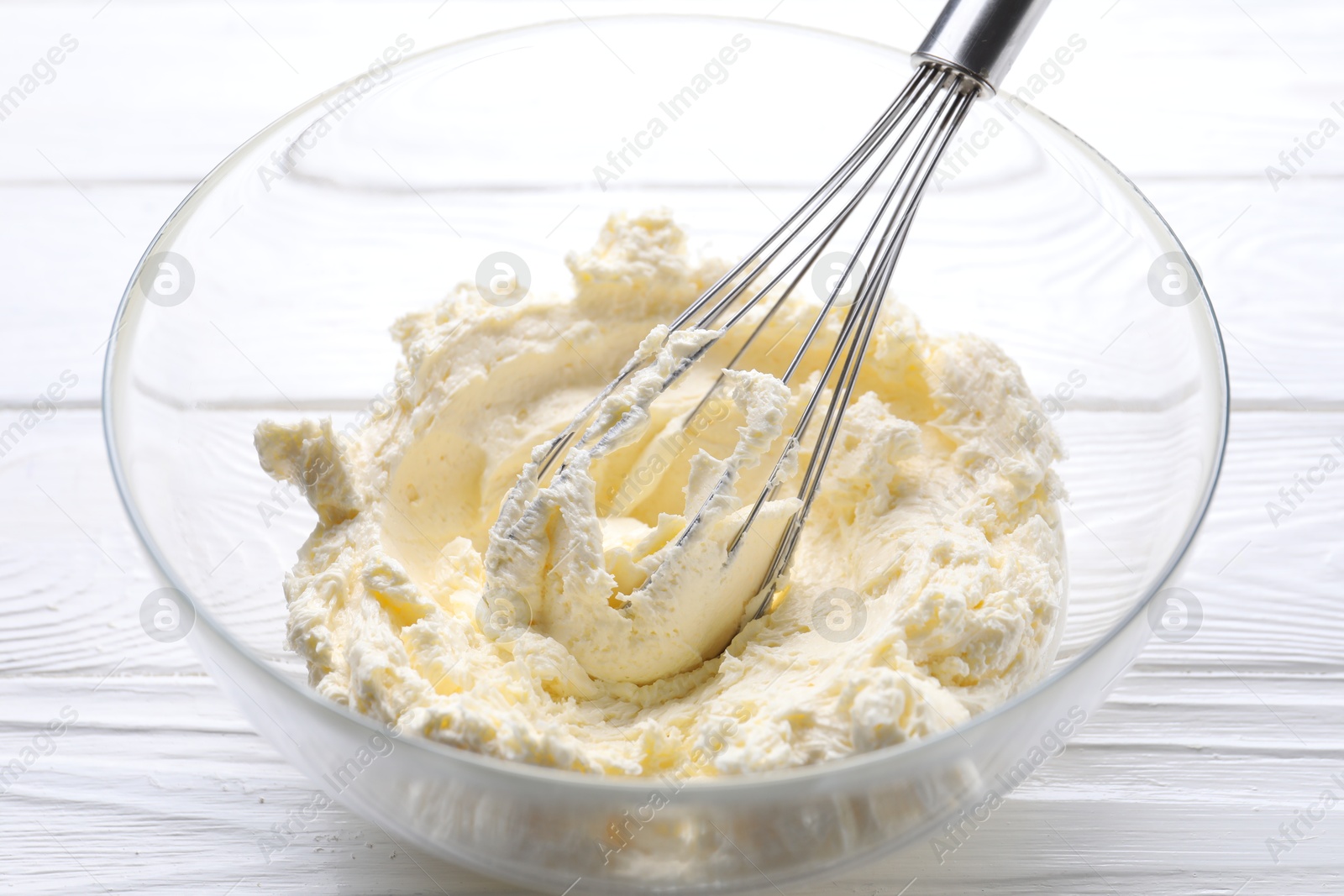 Photo of Bowl with whisk and whipped cream on white wooden table, closeup