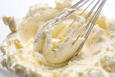 Photo of Whisk and whipped cream in bowl, closeup