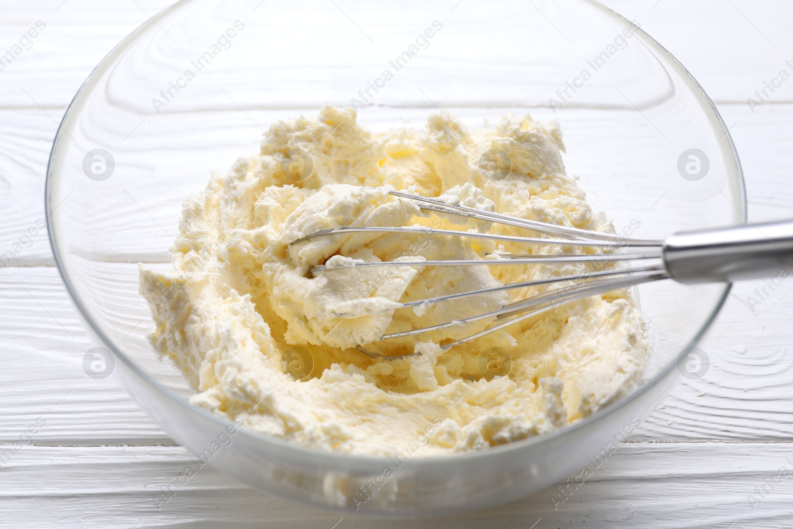 Photo of Bowl with whisk and whipped cream on white wooden table, closeup