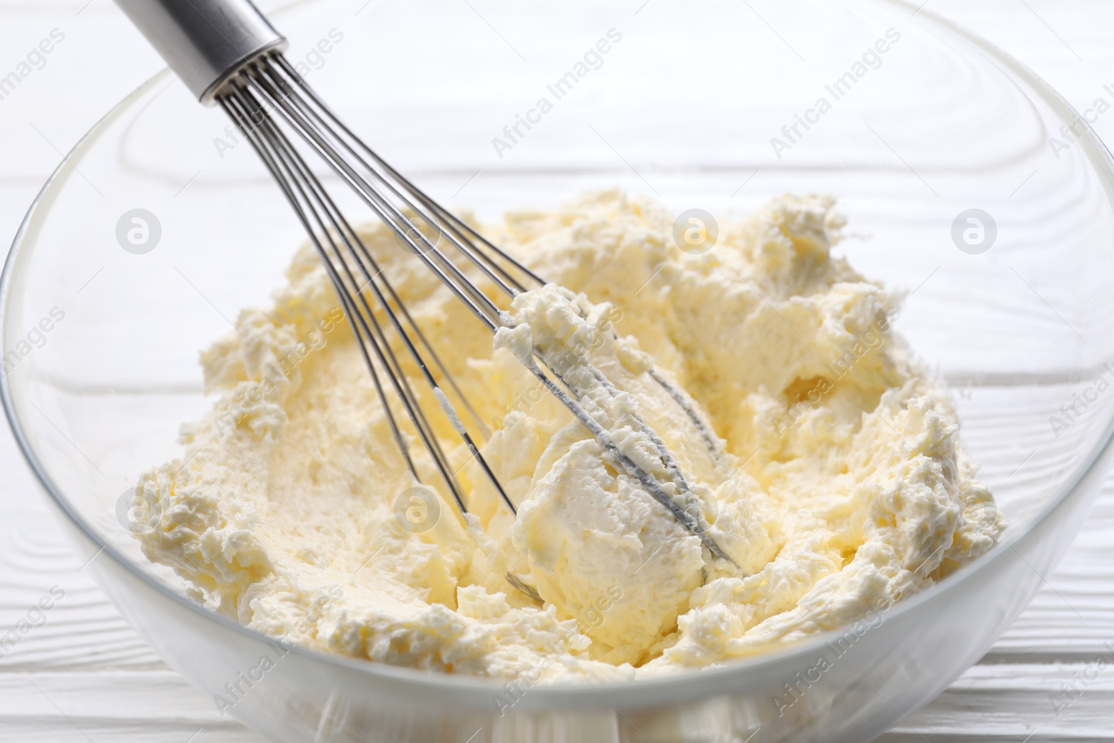 Photo of Bowl with whisk and whipped cream on white wooden table, closeup