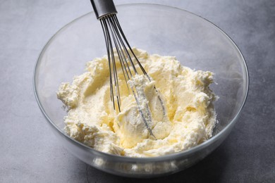 Photo of Bowl with whisk and whipped cream on grey table, closeup