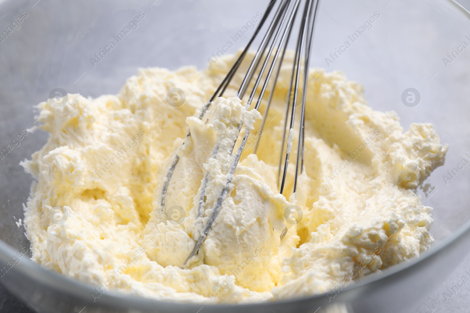 Photo of Bowl with whisk and whipped cream on grey table, closeup