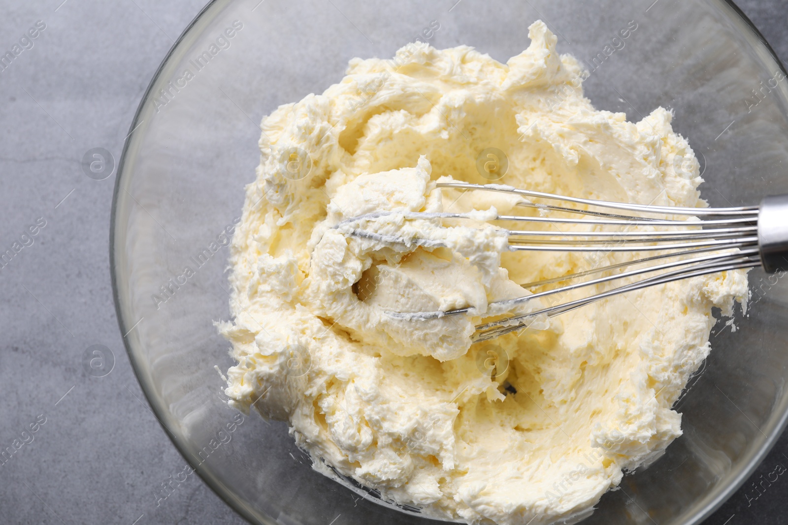 Photo of Bowl with whisk and whipped cream on grey table, top view