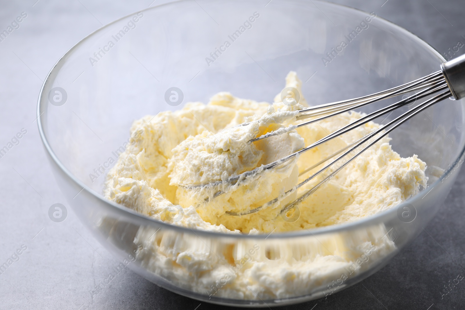 Photo of Bowl with whisk and whipped cream on grey table, closeup