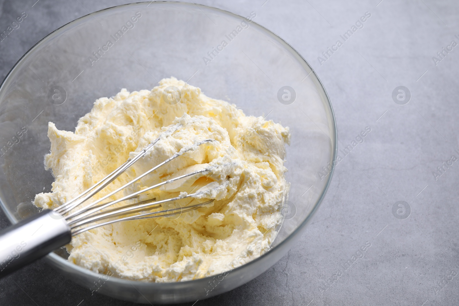 Photo of Bowl with whisk and whipped cream on grey table, closeup. Space for text