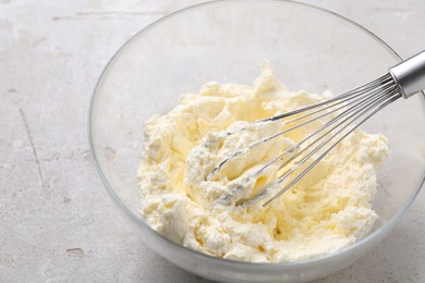 Photo of Bowl with whisk and whipped cream on light grey table, closeup