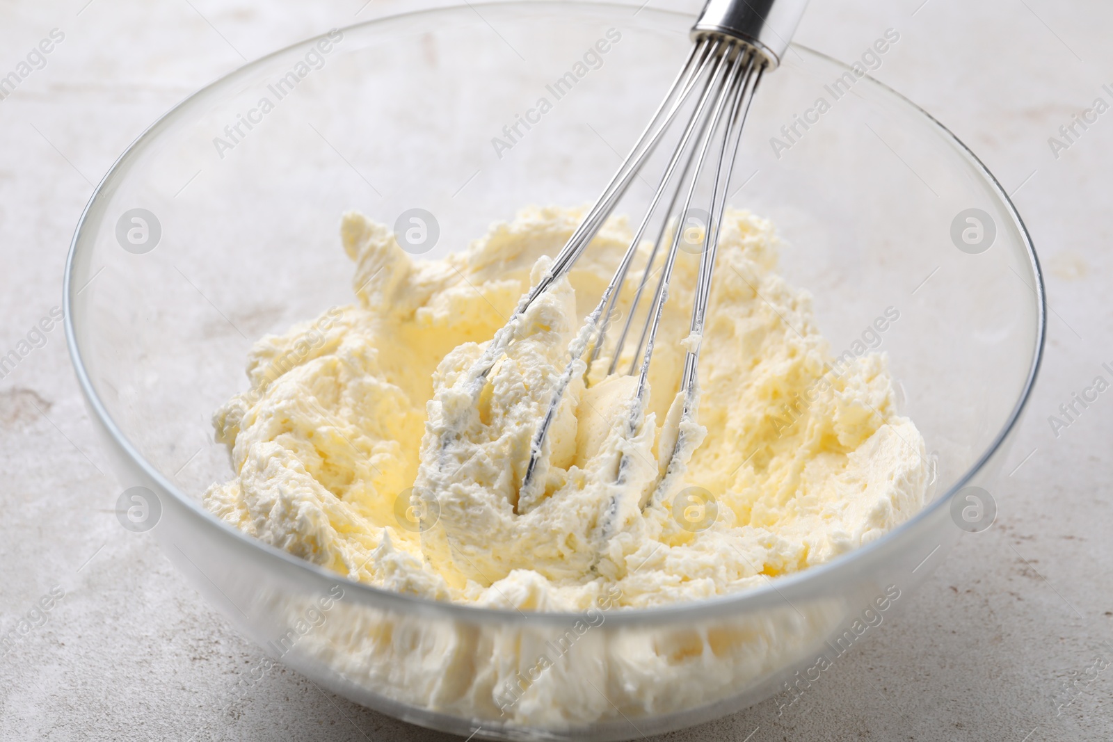 Photo of Whisking whipped cream in bowl on light grey table, closeup