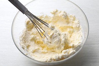 Photo of Bowl with whisk and whipped cream on white wooden table, closeup