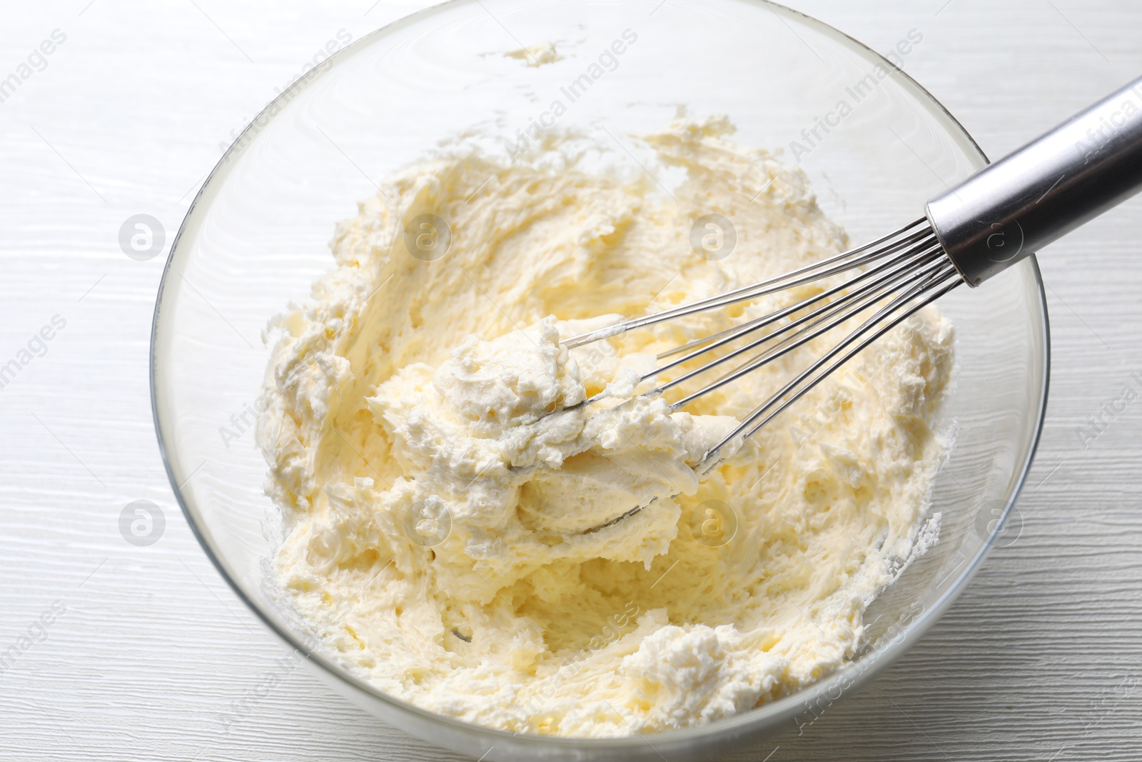 Photo of Bowl with whisk and whipped cream on white wooden table, closeup