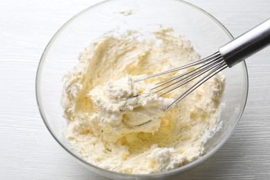 Photo of Bowl with whisk and whipped cream on white wooden table, closeup