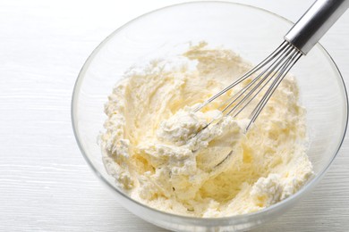 Photo of Bowl with whisk and whipped cream on white wooden table, closeup