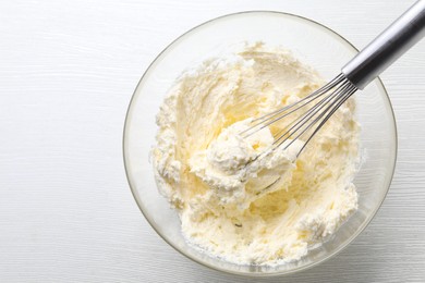 Photo of Bowl with whisk and whipped cream on white wooden table, top view