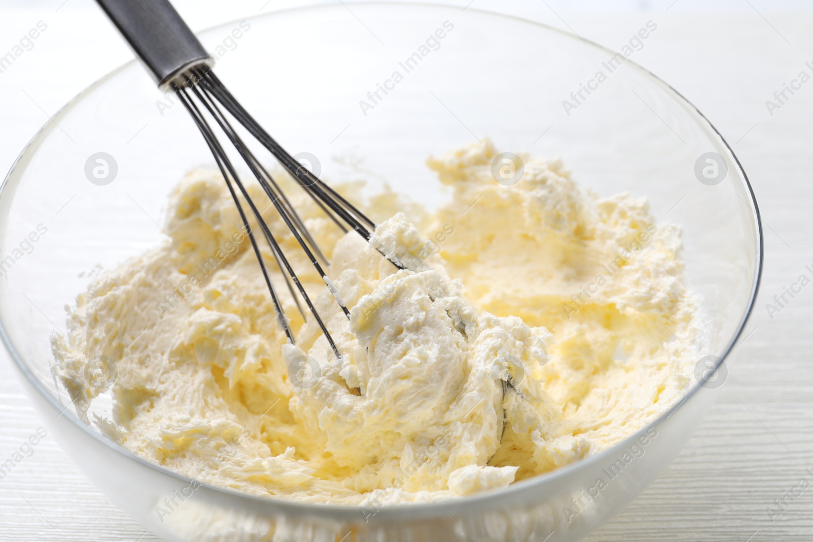 Photo of Bowl with whisk and whipped cream on white wooden table, closeup