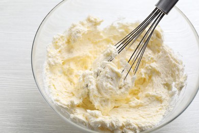 Photo of Bowl with whisk and whipped cream on white wooden table, closeup