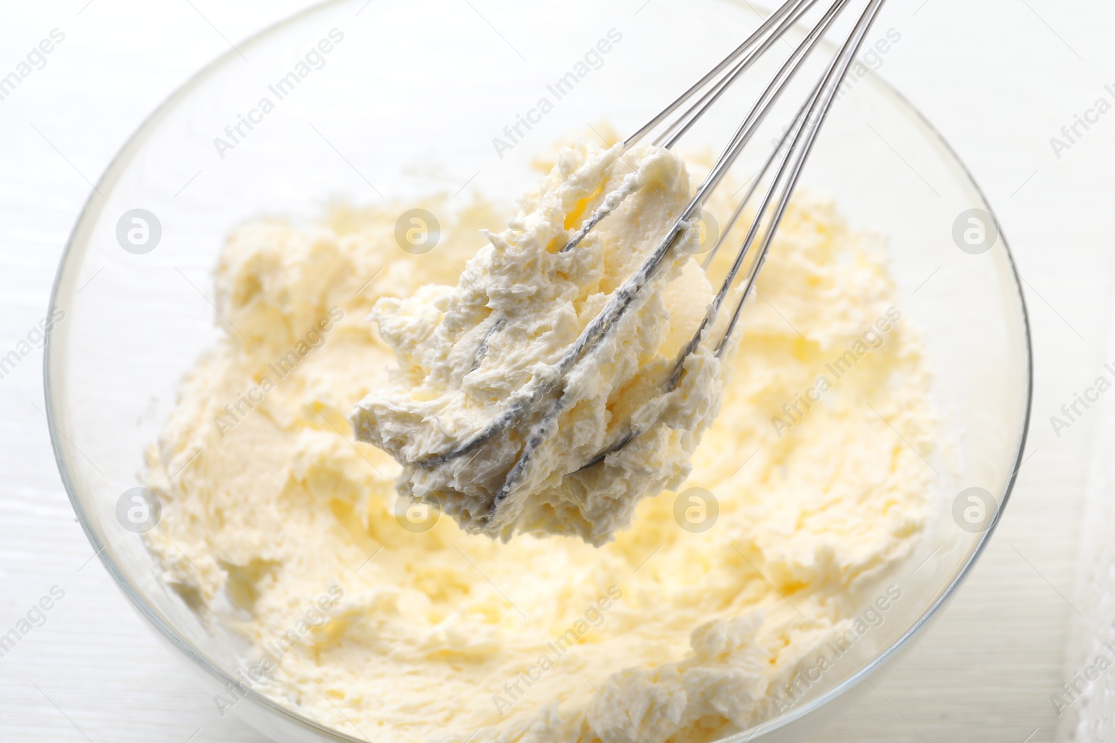 Photo of Bowl with whisk and whipped cream on white wooden table, closeup