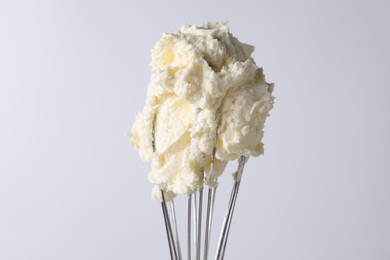 Photo of Whisk with whipped cream on white background, closeup