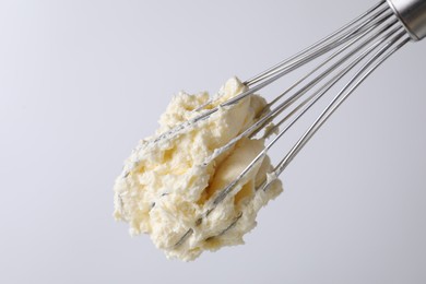 Photo of Whisk with whipped cream on white background, closeup