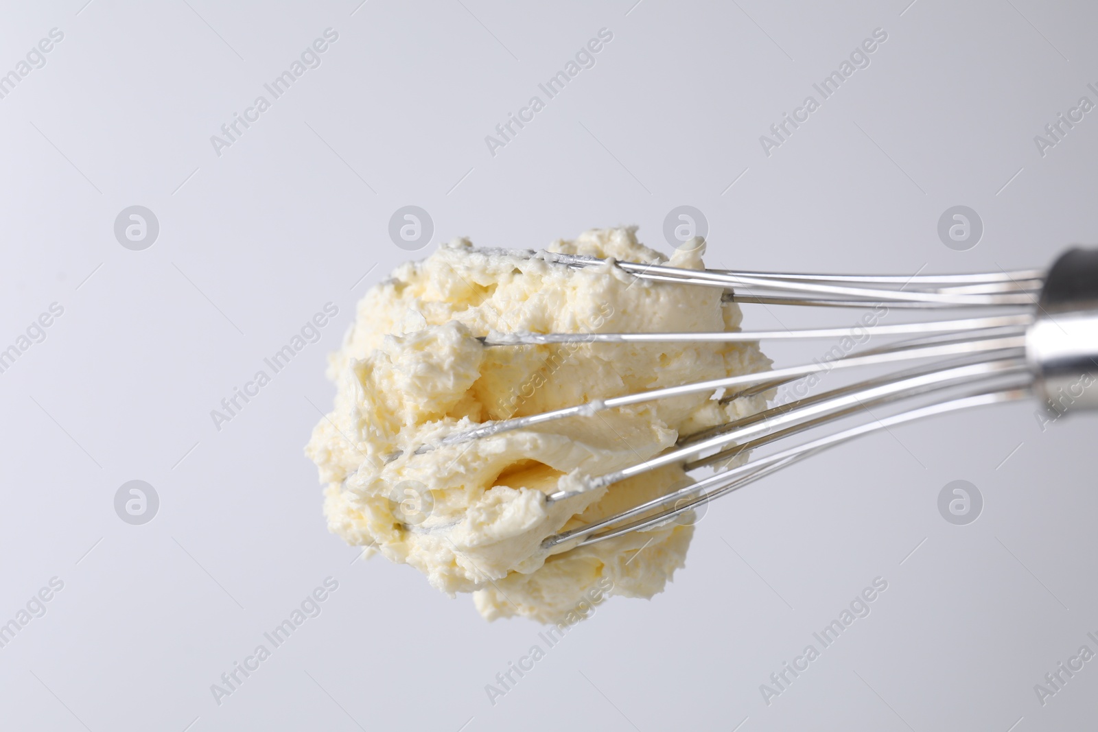 Photo of Whisk with whipped cream on white background, closeup