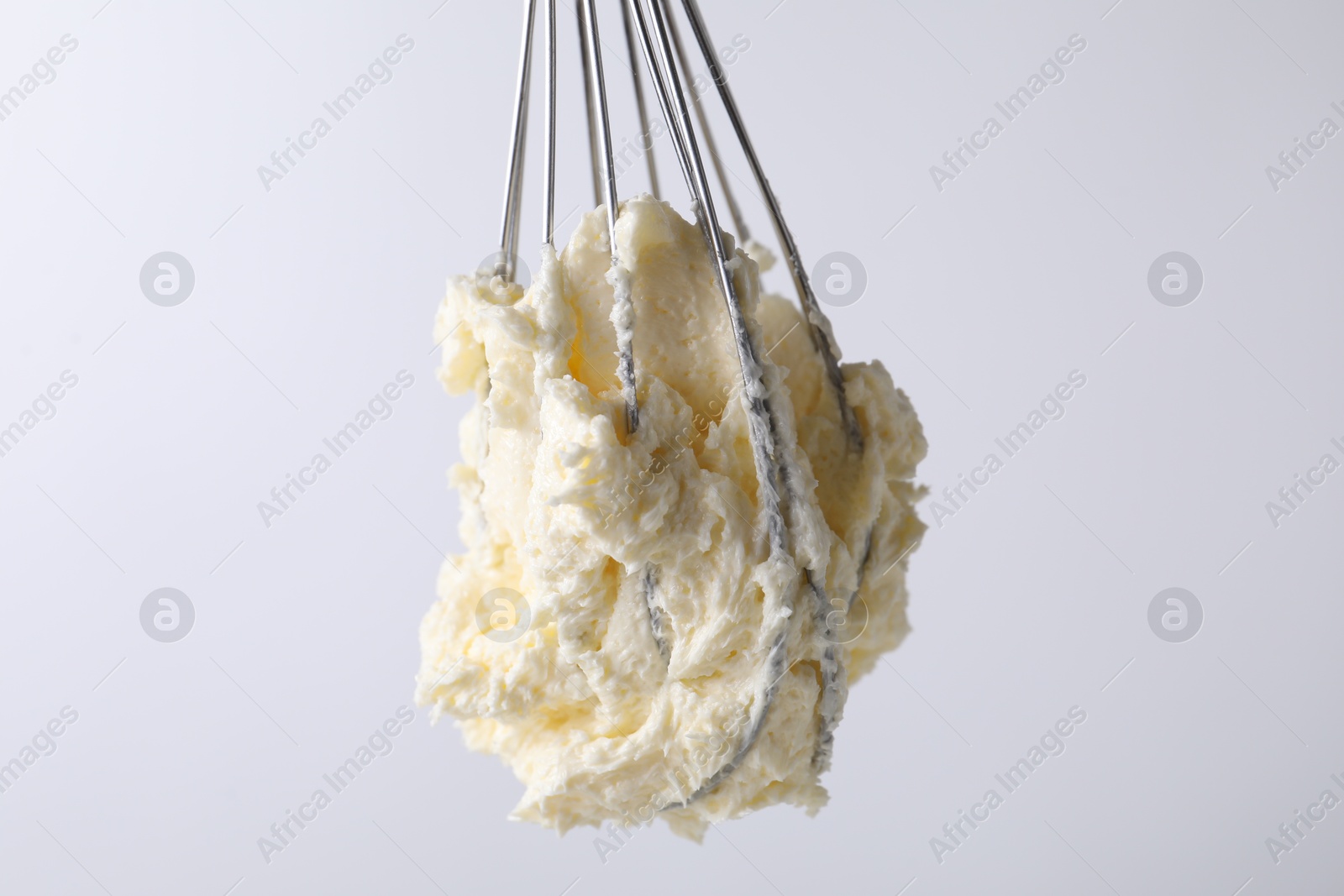 Photo of Whisk with whipped cream on white background, closeup